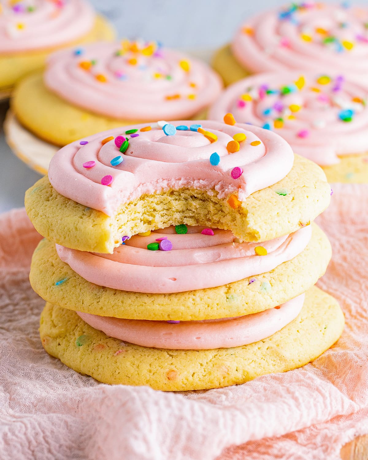 A stack of pink frosted sugar cookies with a bite out of the top cookie.