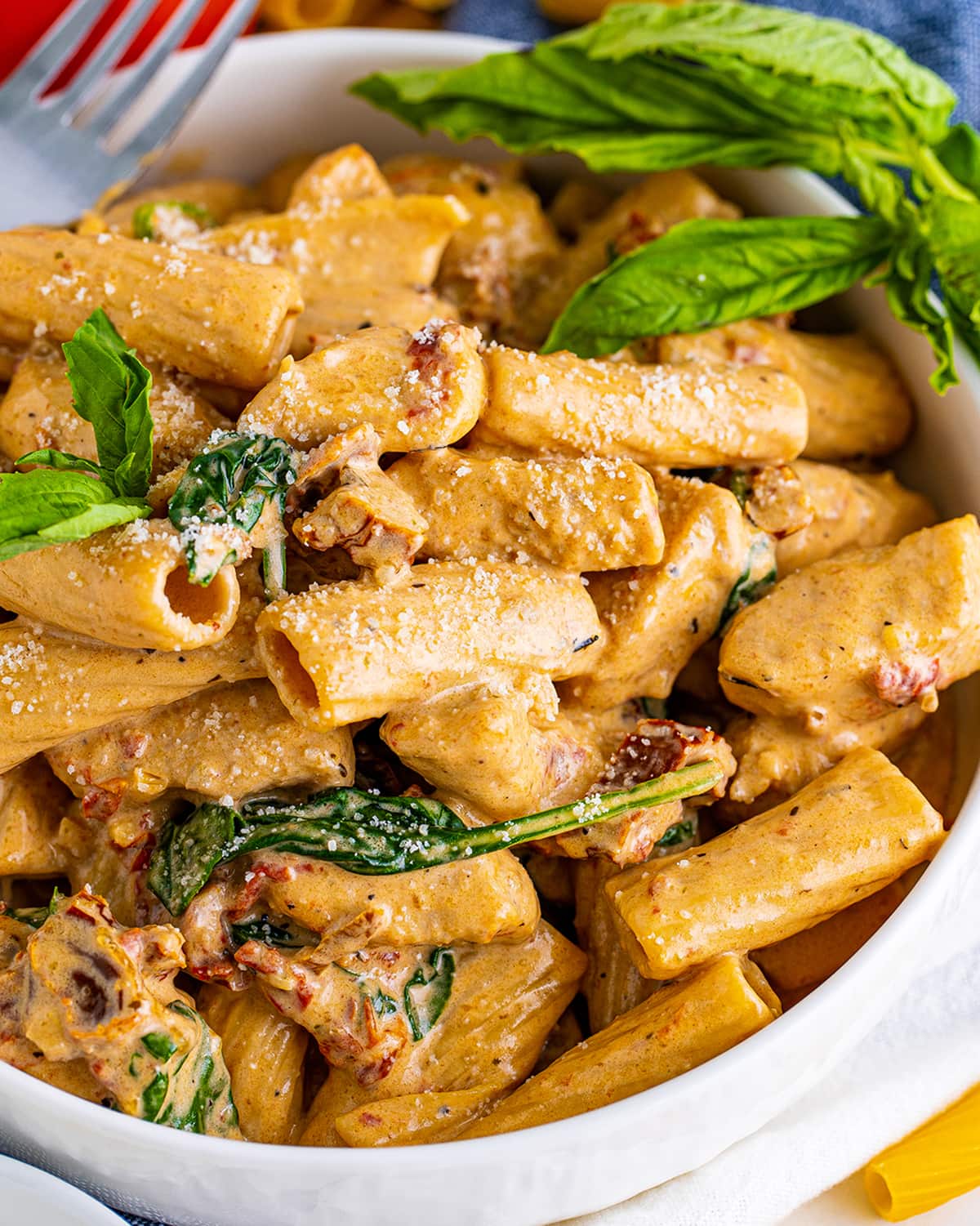 A close up of a bowl of tuscan chicken pasta topped with fresh basil.