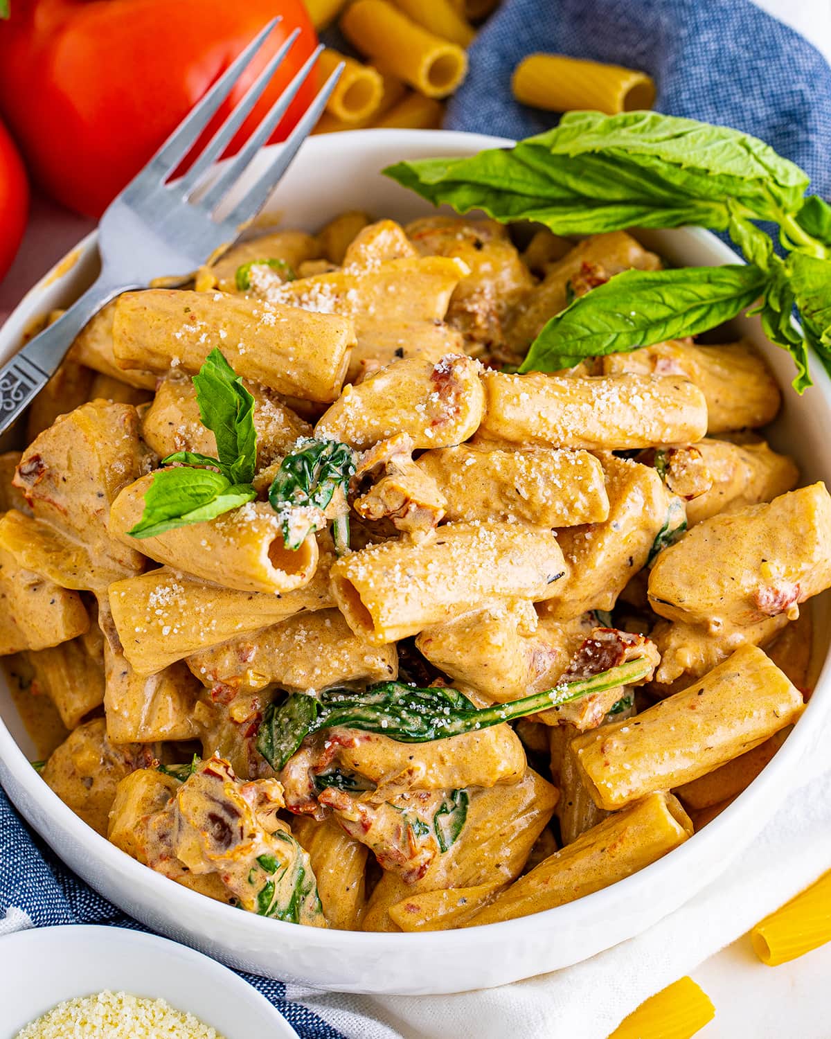 A bowl of creamy sundried tomato chicken pasta topped with a fork and basil leaves.