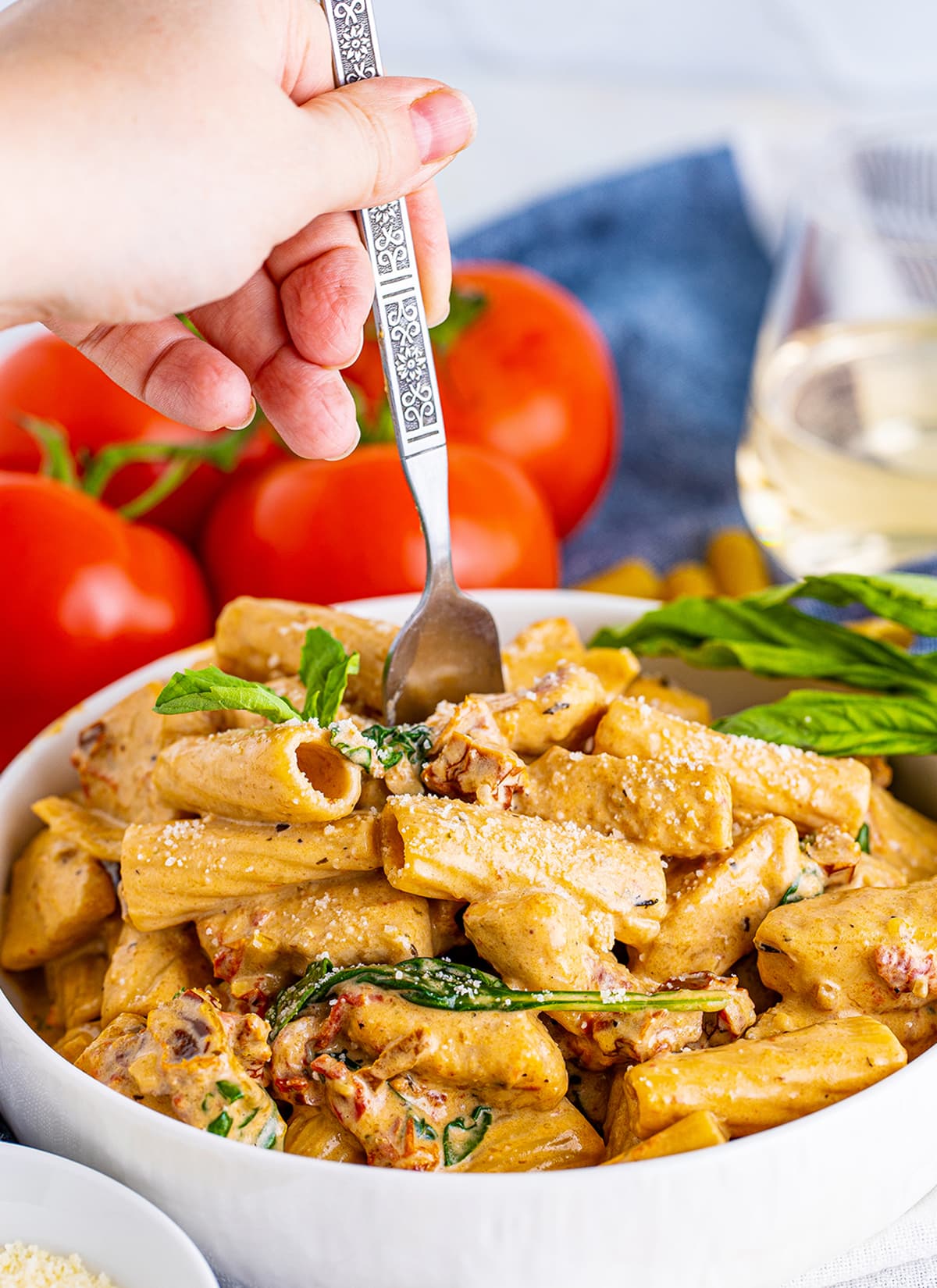 A bowl of creamy tuscan chicken pasta with a hand holding a fork in it.