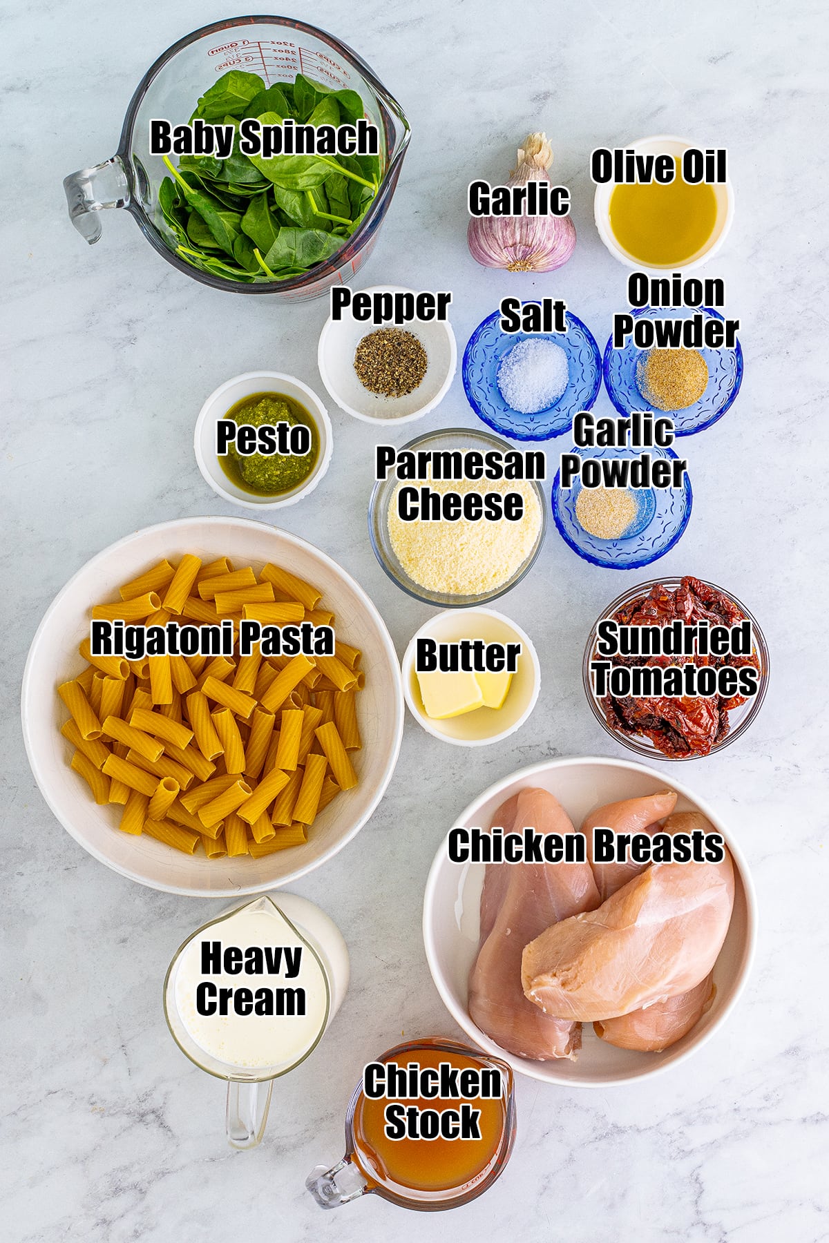 An overhead photo of the ingredients needed to make Tuscan chicken pasta in bowls, with labels on them. 