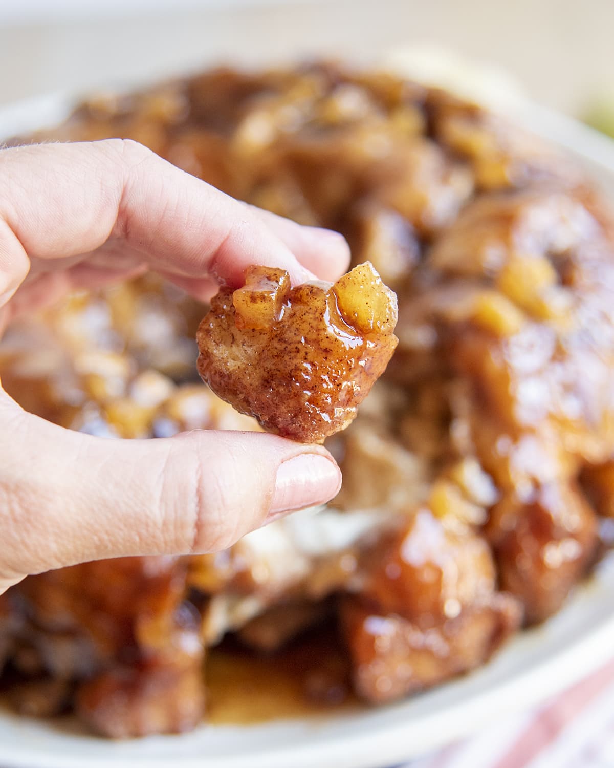 A hand holding a piece of monkey bread with small apple pieces on it.