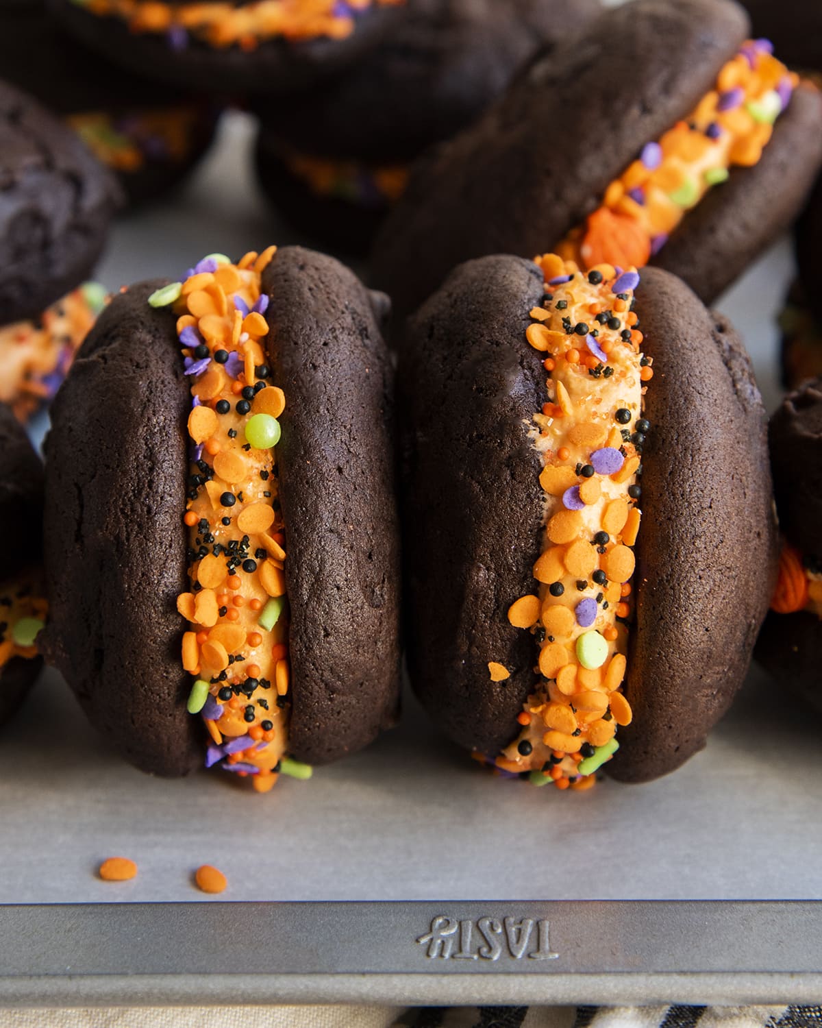 Two orange frosting filled chocolate whoopie pies on their side with a thick layer of frosting between them.