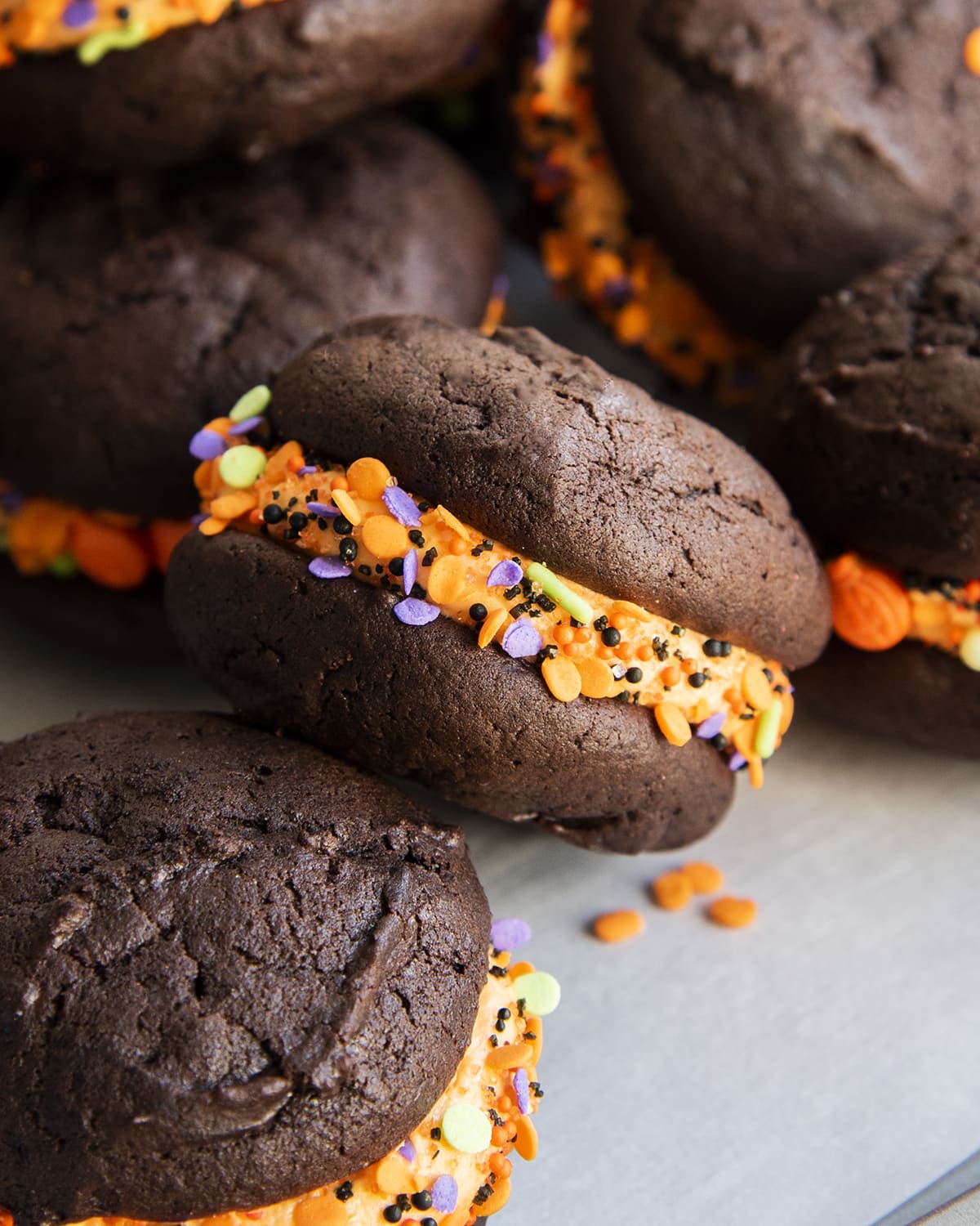 A chocolate cookie sandwich with orange frosting and orange sprinkles in the middle.