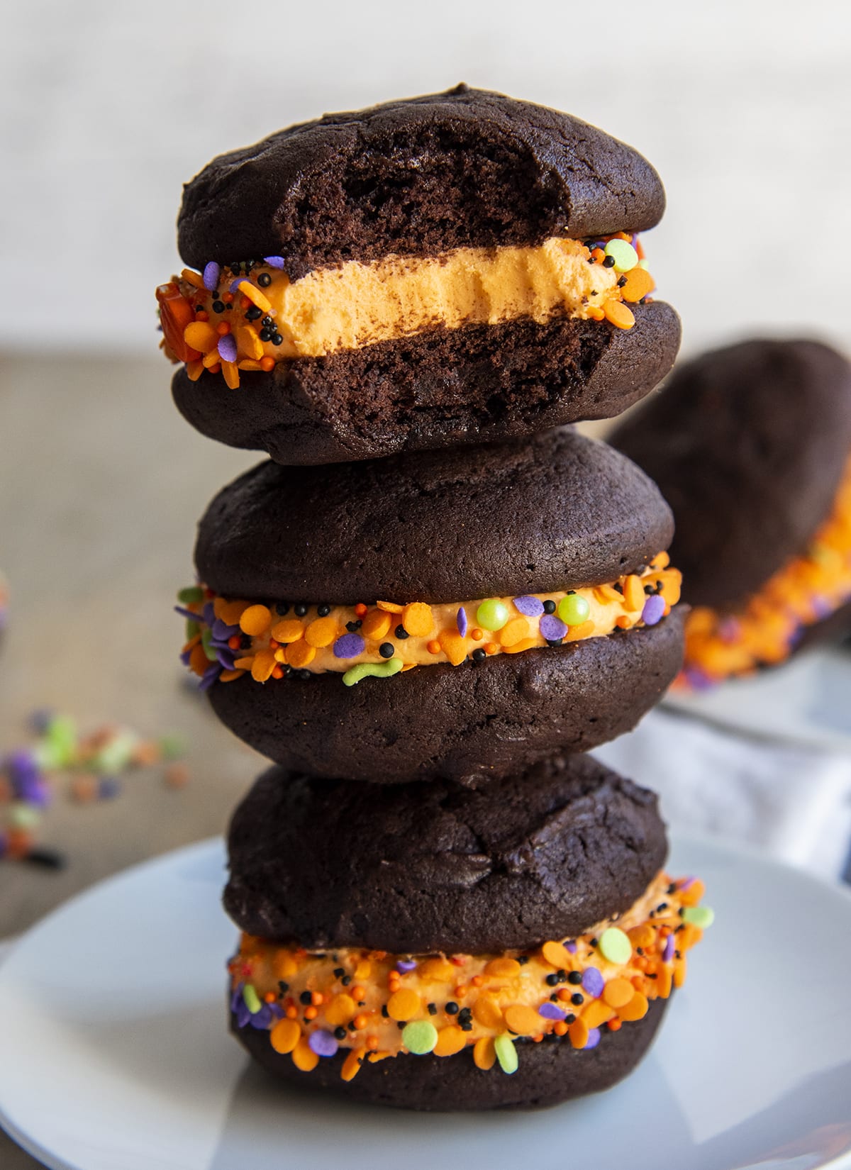 A stack of three chocolate Halloween whoopie pie sandwiches on a plate, with a bite out of the top sandwich.