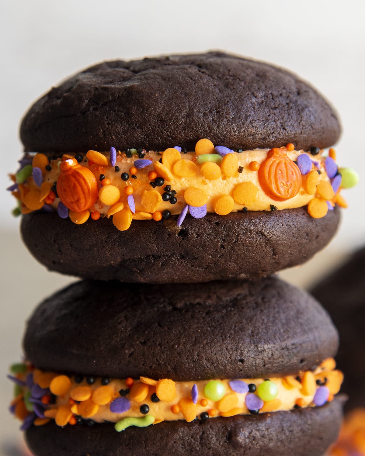 A close up of a chocolate whoopie pie sandwich with orange buttercream and Halloween sprinkles.
