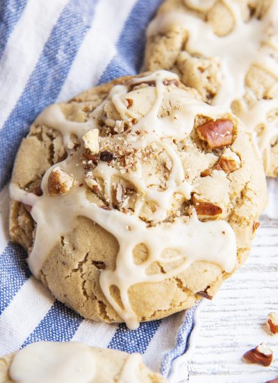 A close up of a maple pecan cookie topped with randomly drizzled maple icing, and chopped pecans.