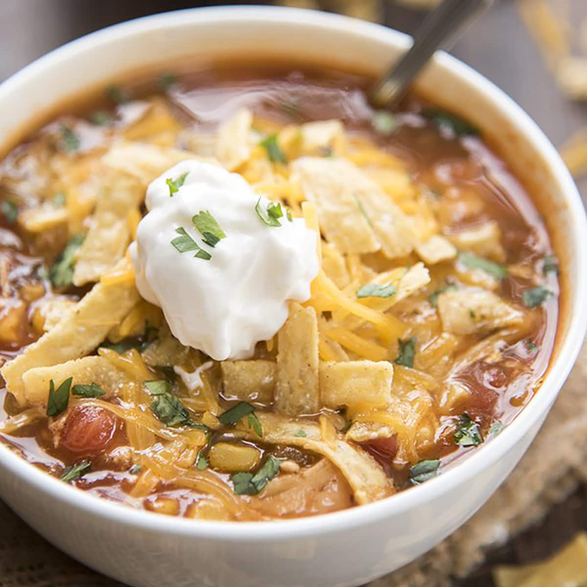 A close up of a bowl of soup topped with tortilla strips, cheese, and a dollop of sour cream.