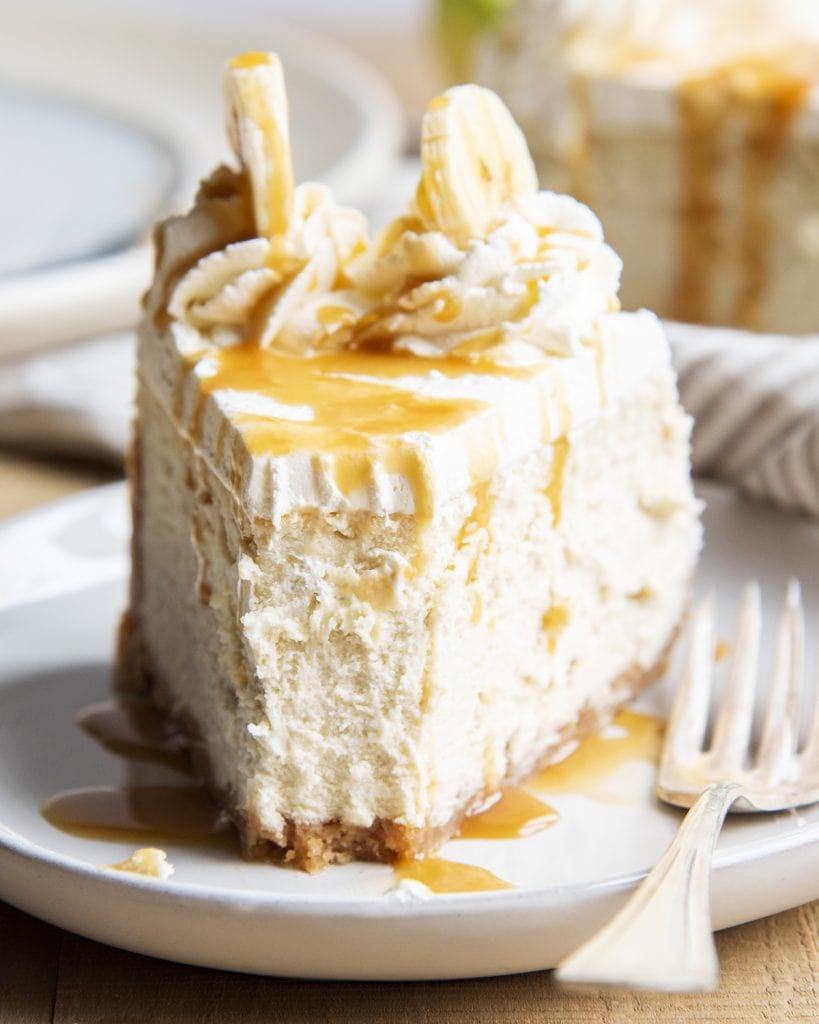 A slice of banana cream cheesecake topped with caramel and a bite out of the front.