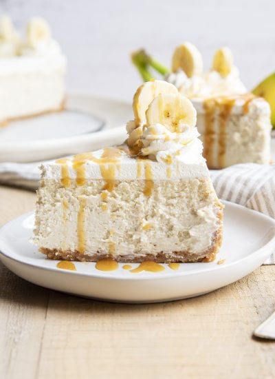 A side view of a slice of banana cheesecake with whipped cream and caramel syrup on top.
