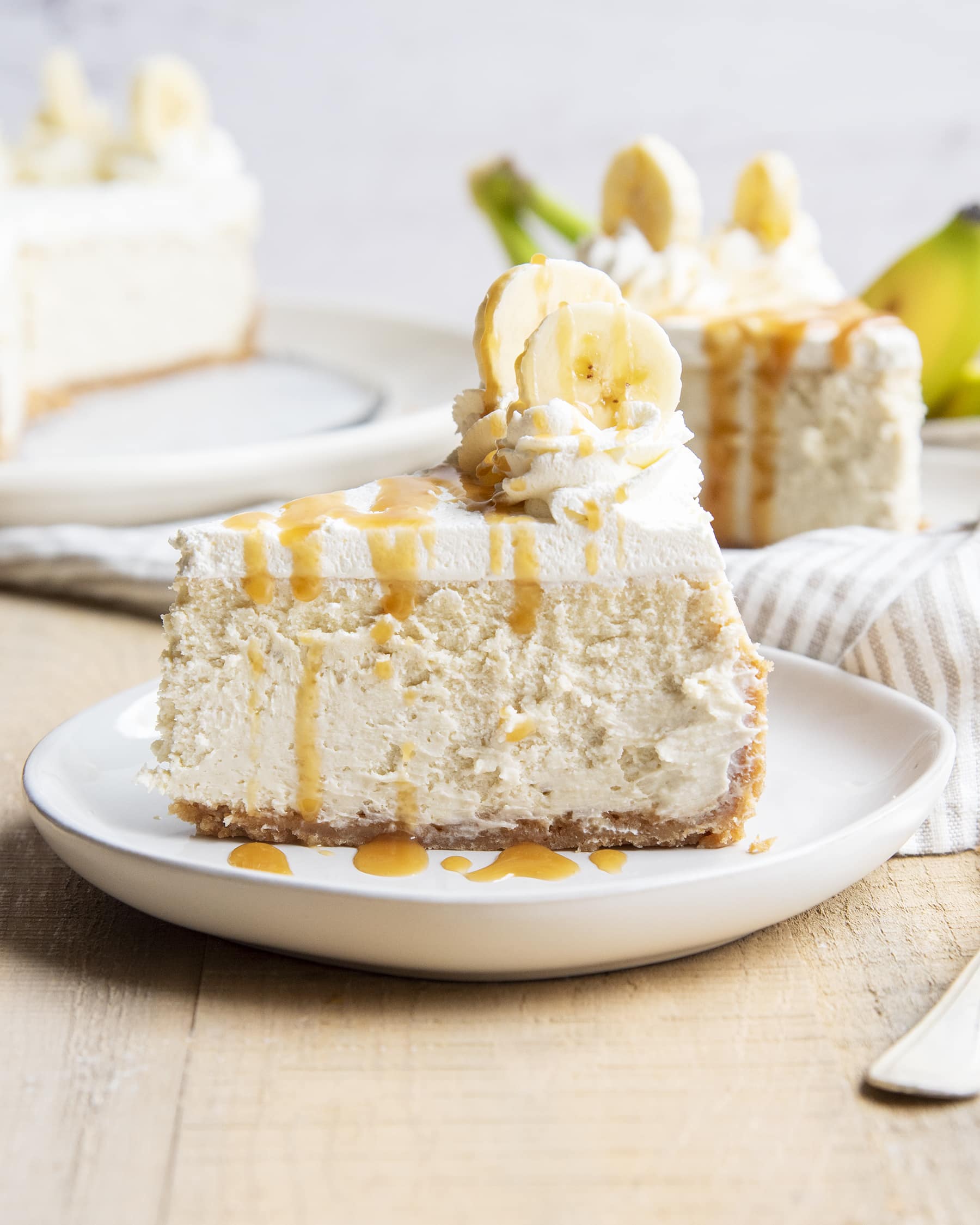 A side view of a slice of banana cheesecake with whipped cream and caramel syrup on top.