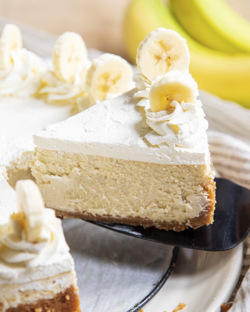 A slice of banana cream cheesecake being lifted out of the cheesecake pan.