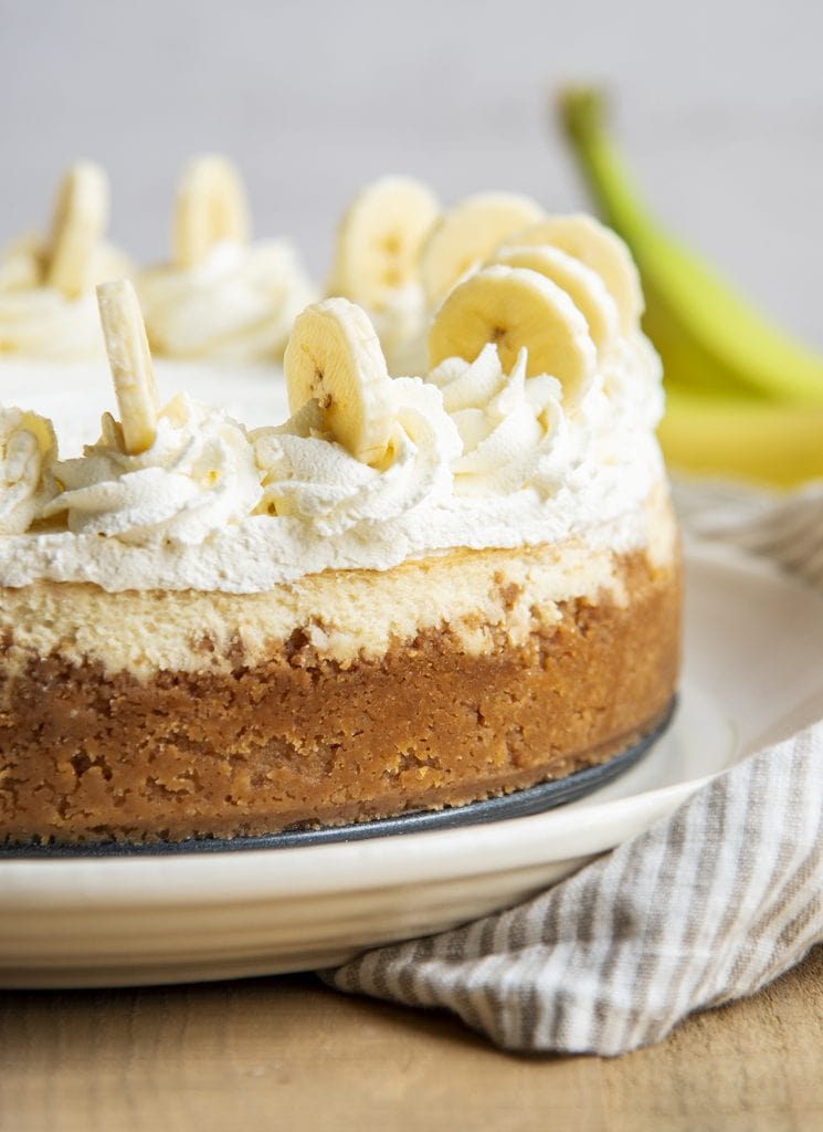 A banana cheesecake with a Vanilla Wafer crust up the sides, and topped with whipped cream dollops and banana slices.