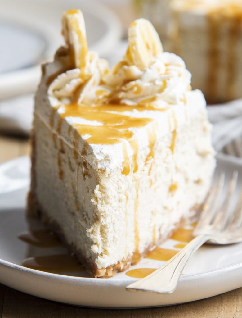 A slice of banana cream cheesecake on a plate topped with whipped cream and caramel syrup.