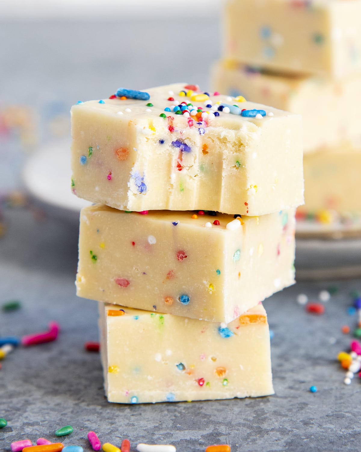 A stack of three pieces of cake batter fudge full of sprinkles with a bite out of the top piece. 
