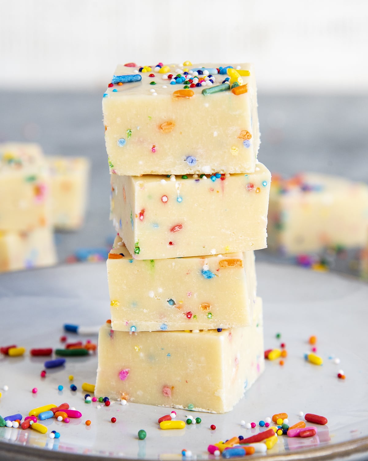 A stack of four pieces of a white cake batter fudge full of funfetti sprinkles.