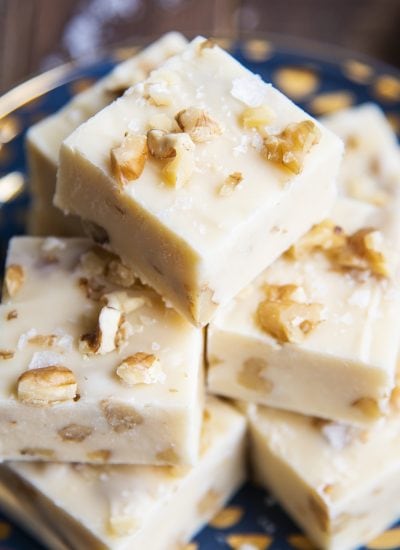 A close up of a pile of maple fudge pieces full of walnuts and topped with flaky sea salt.