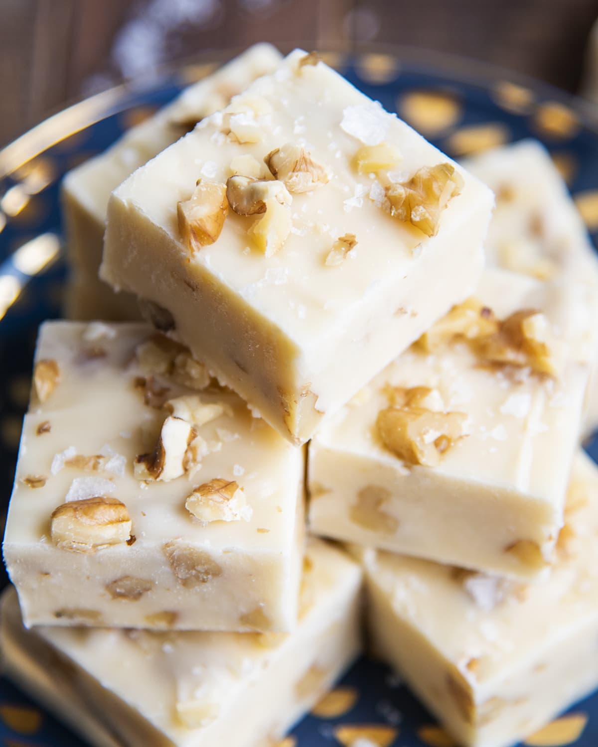 A close up of a pile of maple fudge pieces full of walnuts and topped with flaky sea salt.