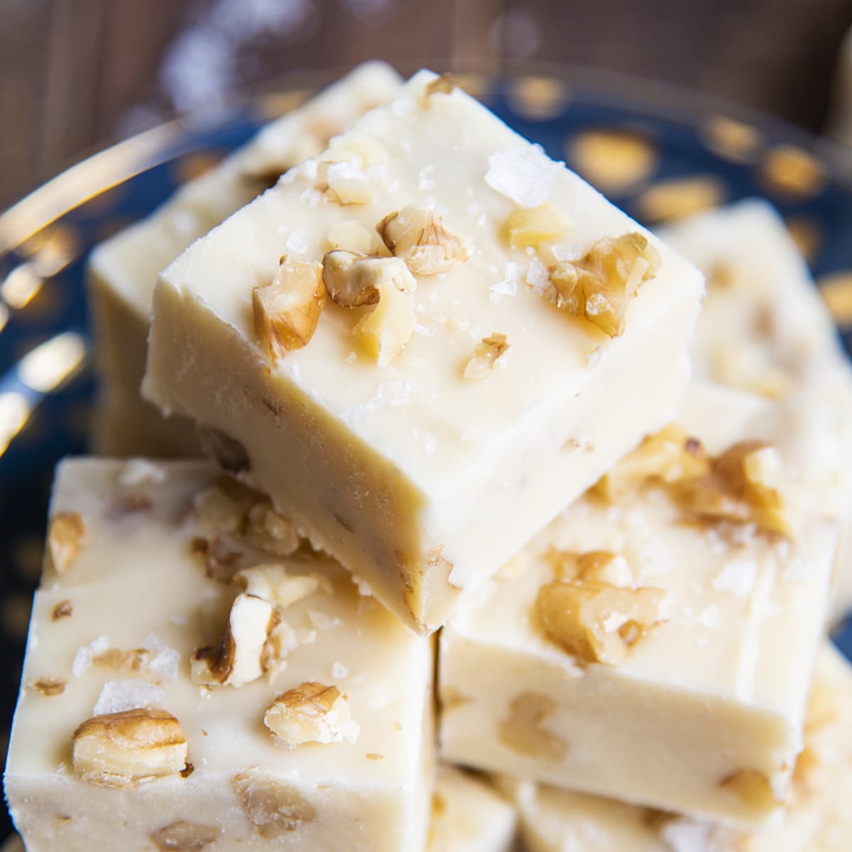 A square close up photo of a piece of maple walnut fudge on a pile of more pieces.
