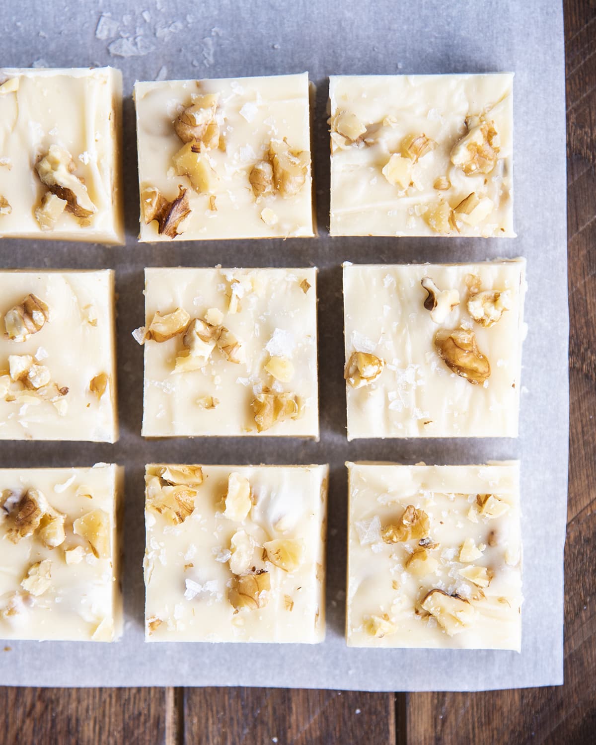 Rows of white chocolate maple walnut fudge on a piece of parchment paper.