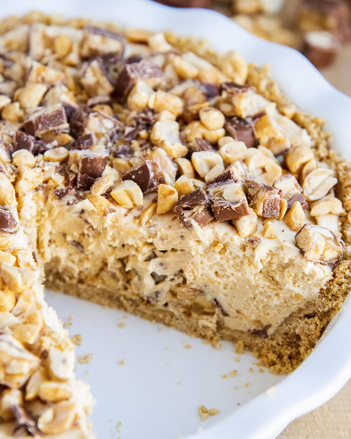A peanut butter snickers pie in a pie pan showing the middle of the pie because a piece is cut out.