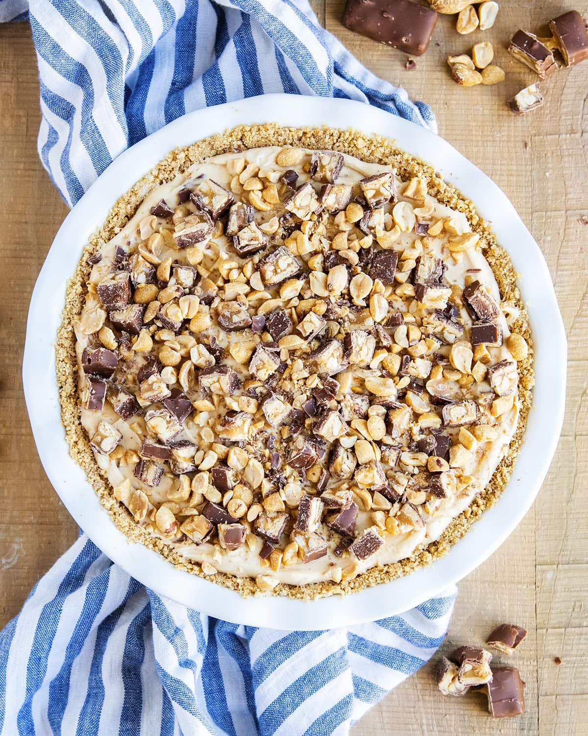 An overhead photo of a no bake snickers pie topped with roasted peanuts and snickers pieces.