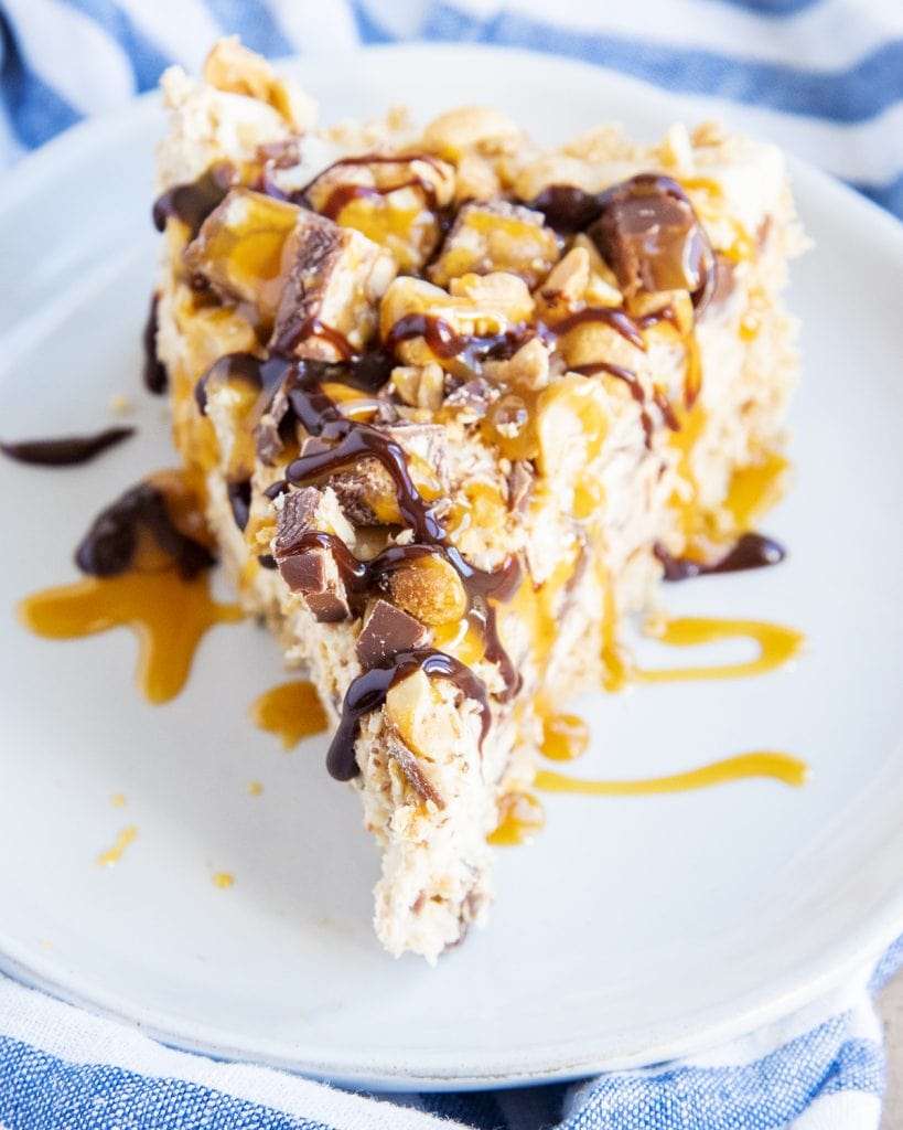 A slice of Snickers Pie on a plate topped with chopped Snickers pieces and peanuts.