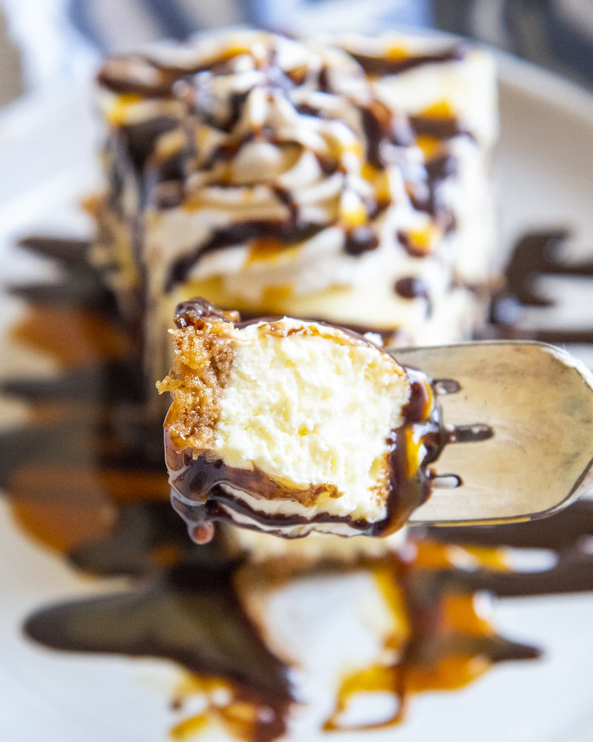 A bite of cheesecake on a fork topped with caramel and chocolate syrup.