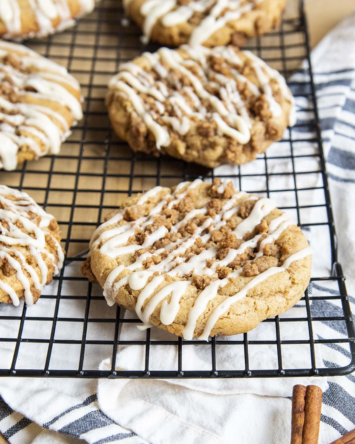 A wire cooling rack topped with giant coffee cake cookies with streusel crumbs, and vanilla icing on top. 