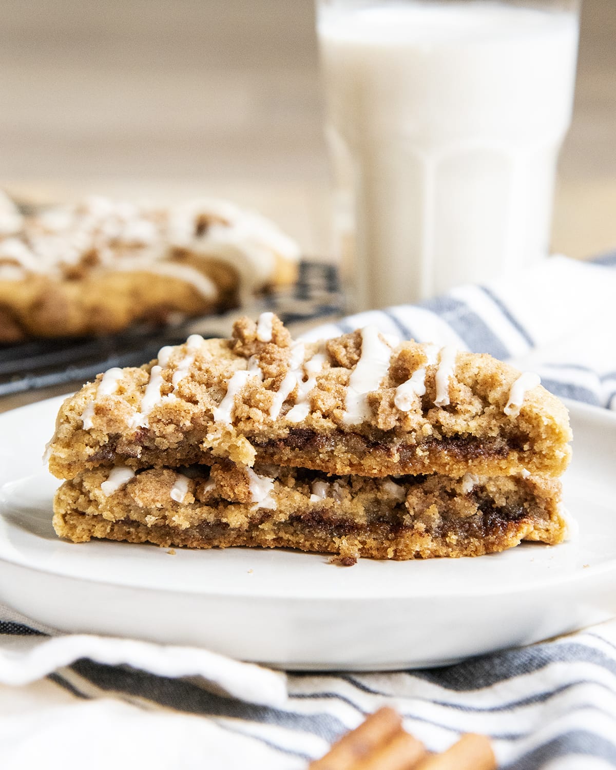 A giant cookie cut open and with a cinnamon swirl, cinnamon streusel, and vanilla icing on top.