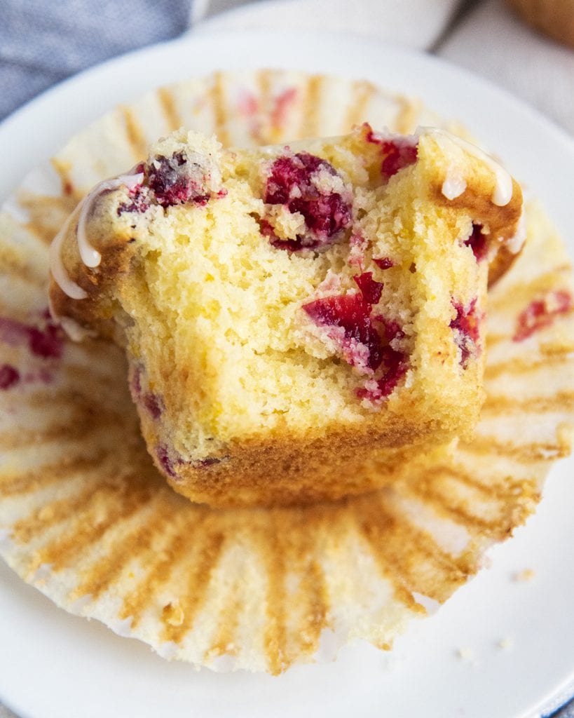 A cranberry orange muffin laying on a muffin liner with a bite out of it.