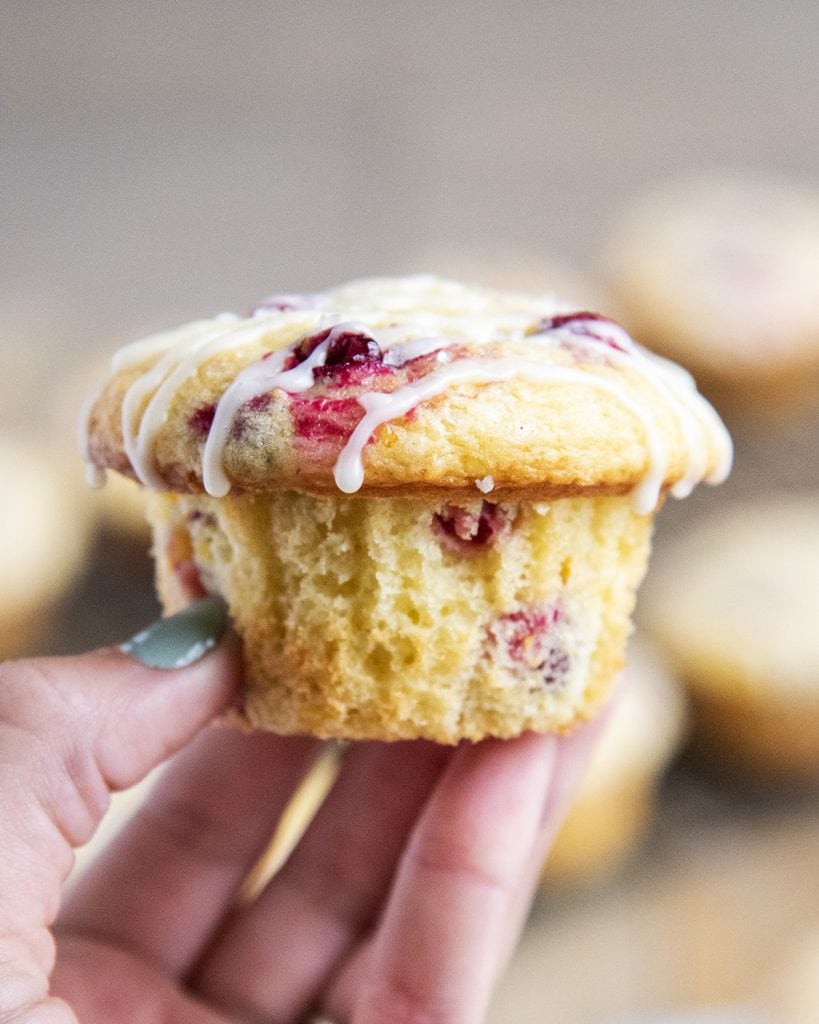 A hand holding a big muffin full of cranberries and with icing drizzled over the top.