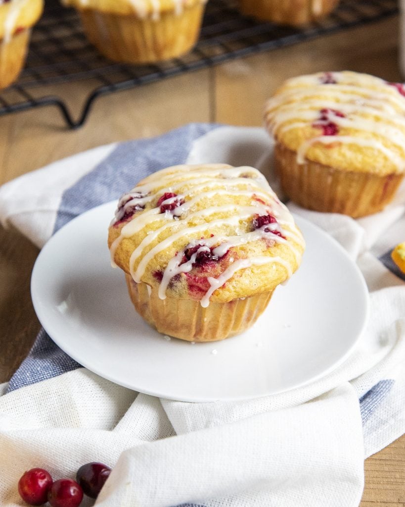 A cranberry orange muffin on a plate with icing drizzled over the top.