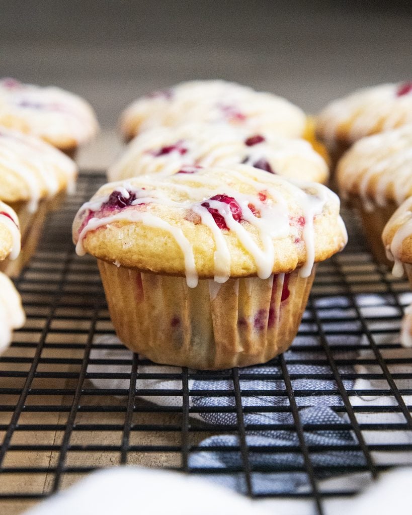 A row of cranberry muffins on a wire cooling rack with orange icing drizzled over the top.