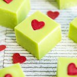 A close up of a square piece of green fudge topped with a heart sprinkle.