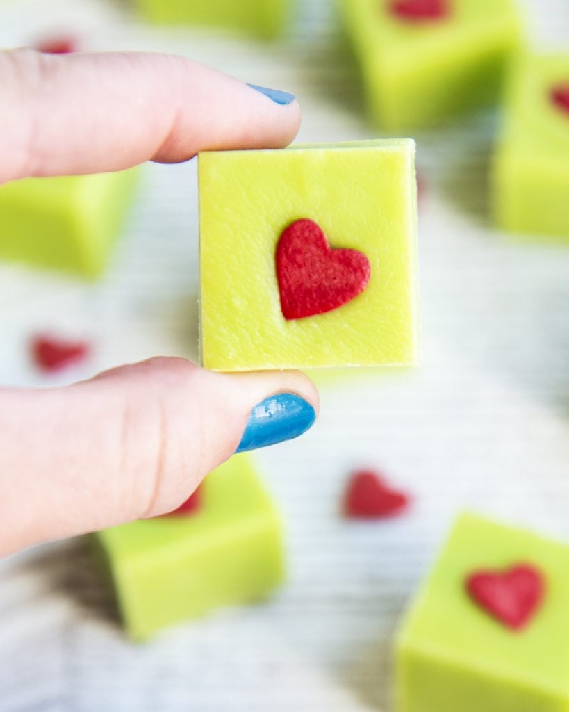 A hang holding a piece of grinch fudge that is green with a red heart sprinkle.