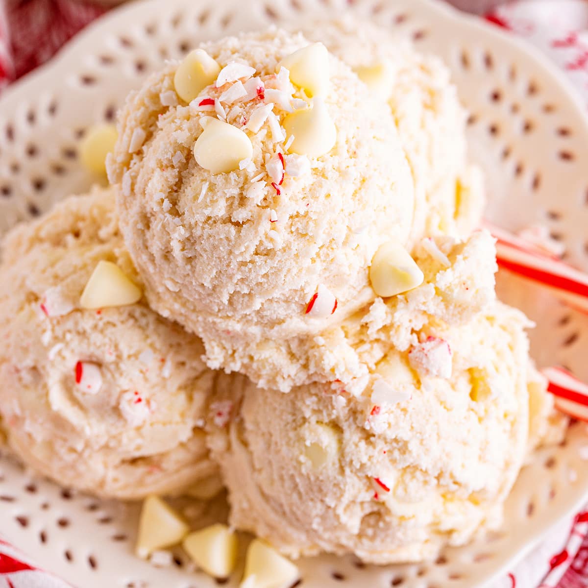 A close up of scoops of peppermint cookie dough with white chocolate chips and candy cane pieces.