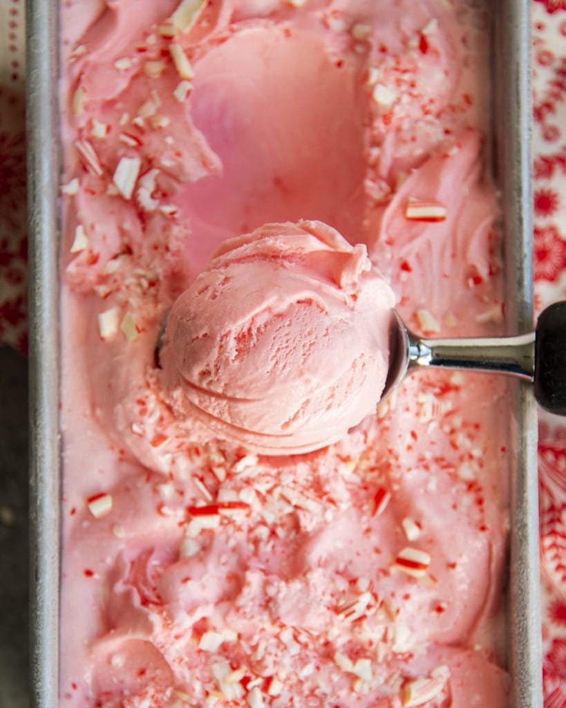A scoop of peppermint ice cream on a container of pink peppermint ice cream.