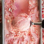 A square image of an overhead photo of a scoop of peppermint ice cream over a container of it.