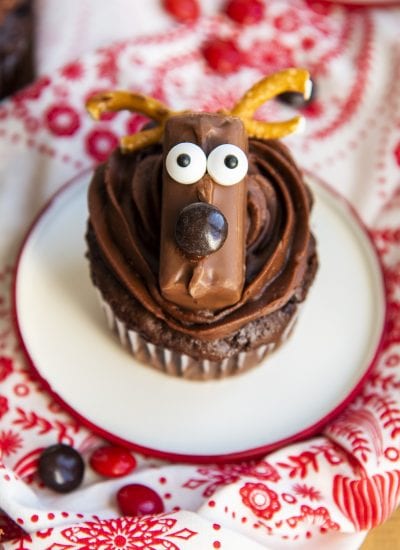 A chocolate cupcake topped with a reindeer with googly eyes and pretzel antlers, and a brown m&m nose.