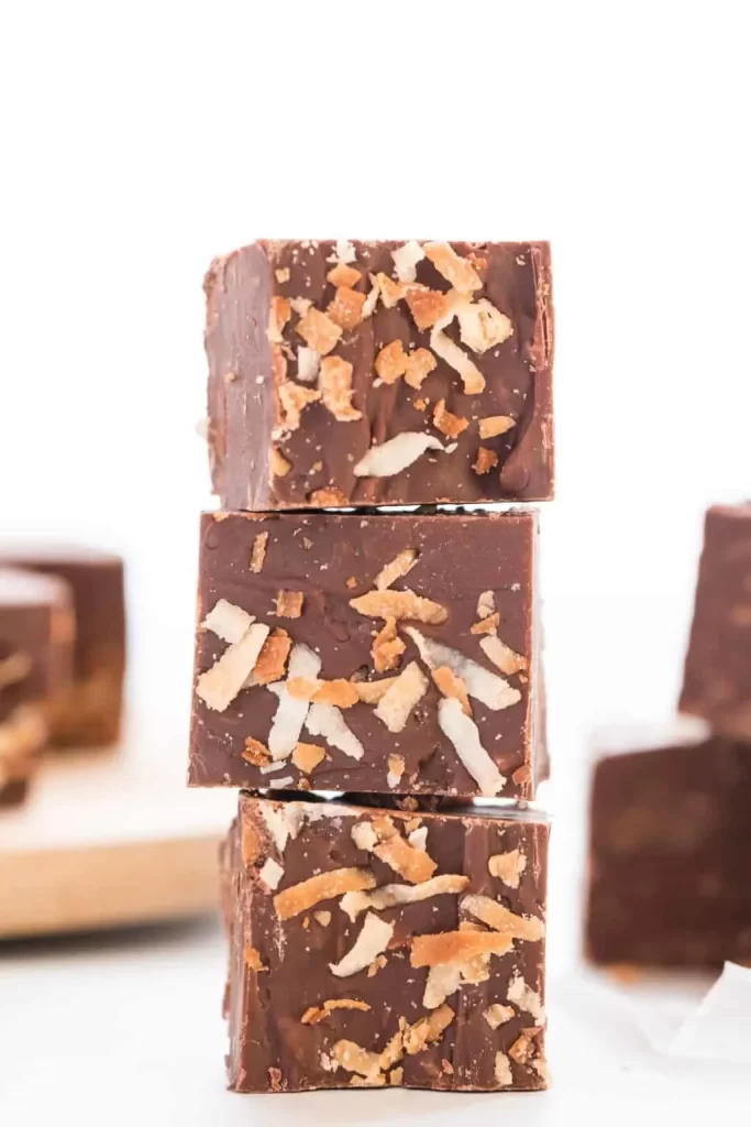 A stack of three pieces of chocolate coconut fudge with toasted coconut on top. 