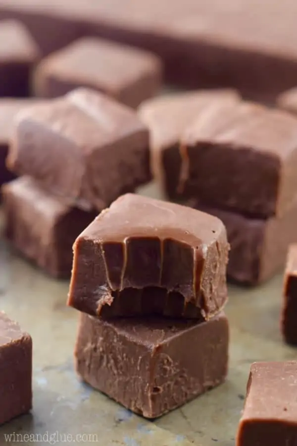 A stack of two pieces of fudge, and the top piece has a bite out of it. 