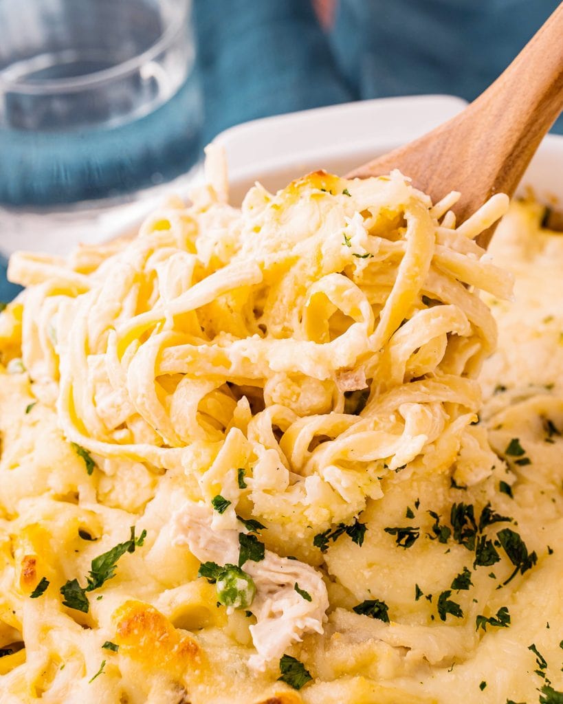 A baking pan with chicken tetrazzini and a wooden spoon in the noodles.