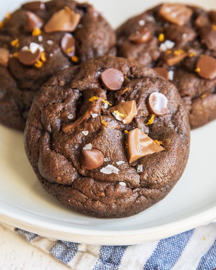 A close up of a chocolate orange cookie with chocolate chips and sea salt on top on a plate.