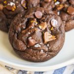 A close up of a chocolate orange cookie with chocolate chips and sea salt on top on a plate.