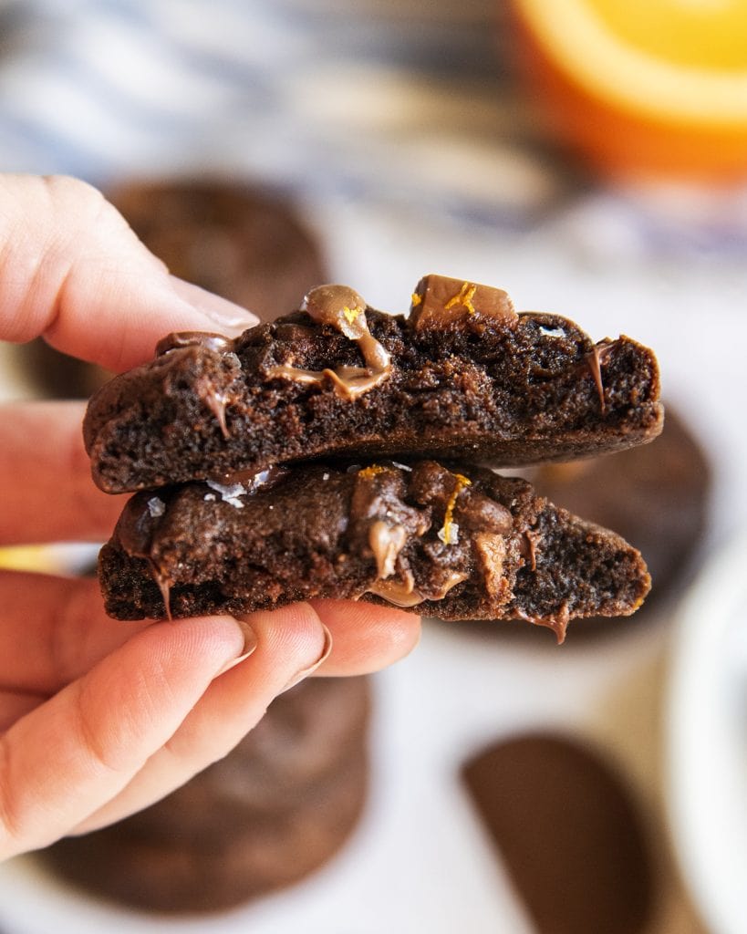 A hand holding two halves of a chocolate cookie, showing the middle of the cookie.