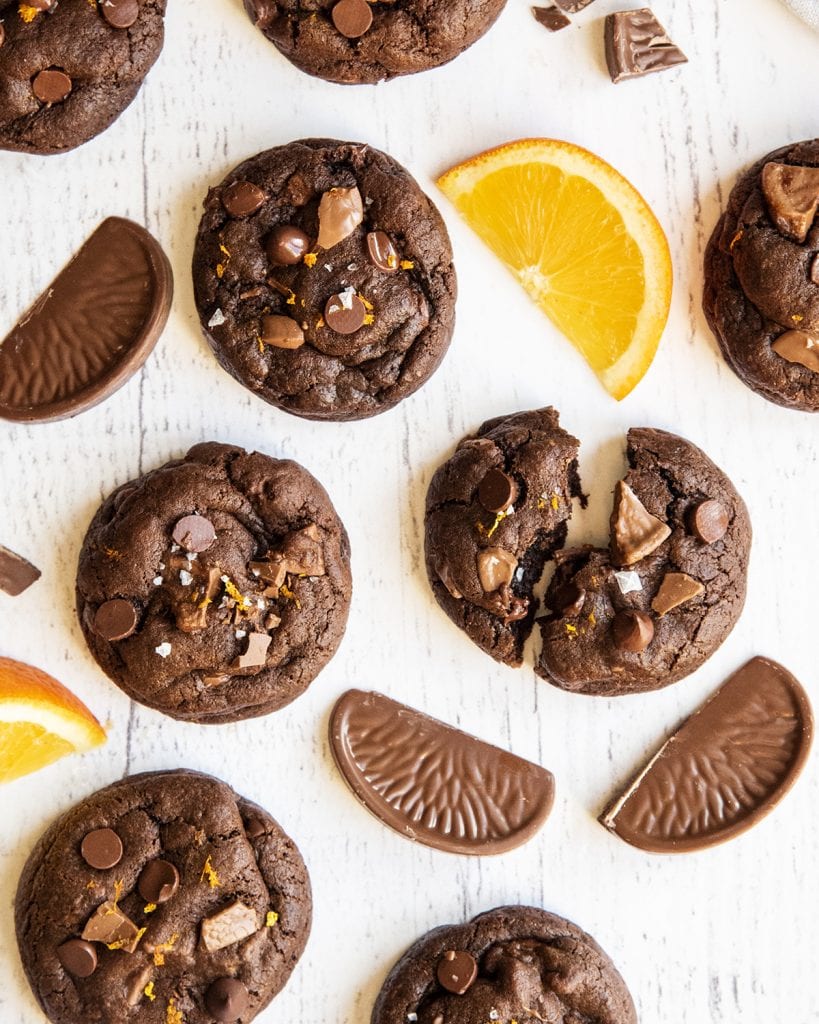 An overhead photo of chocolate orange cookies on a white table with chocolate orange candy slices next to it.