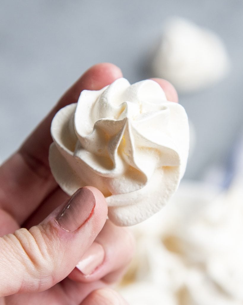 A hand holding a piped white meringue cookie.