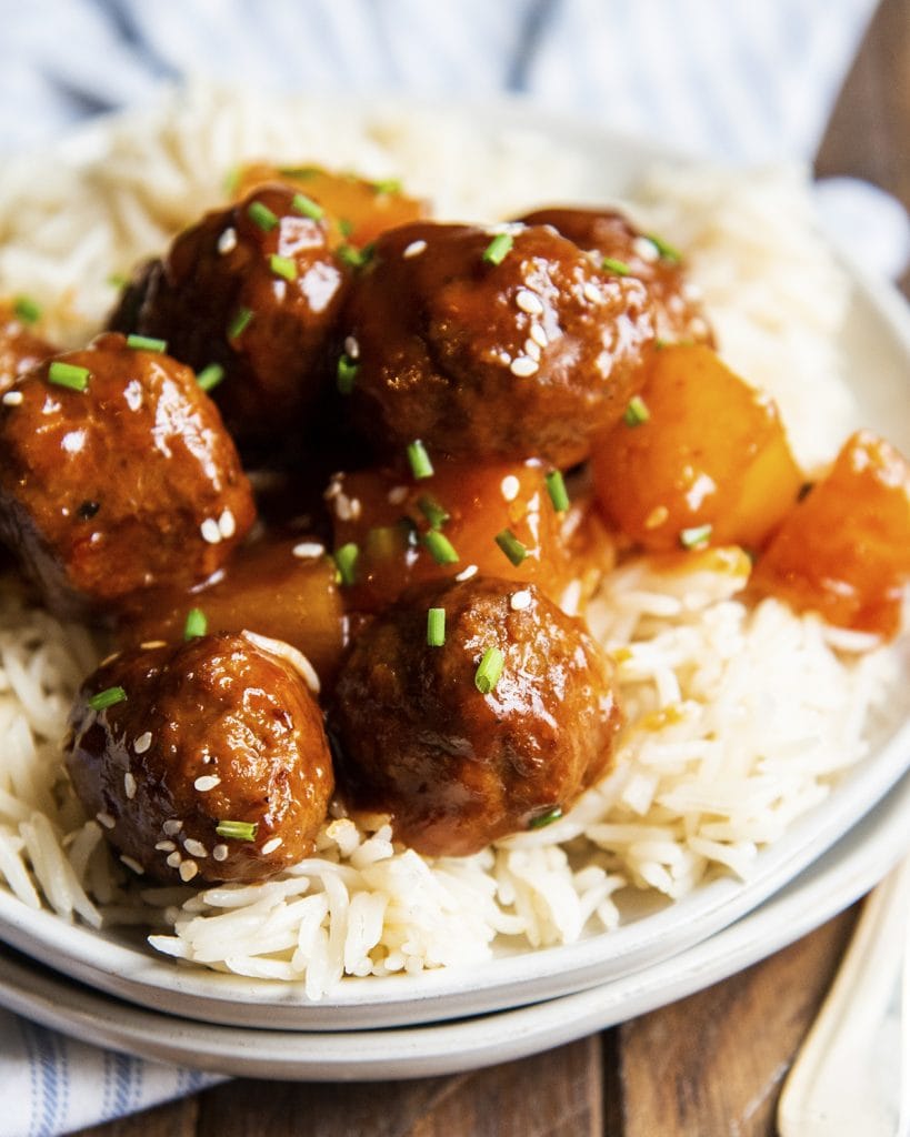 A close up of Hawaiian BBQ meatballs over a bowl of rice.