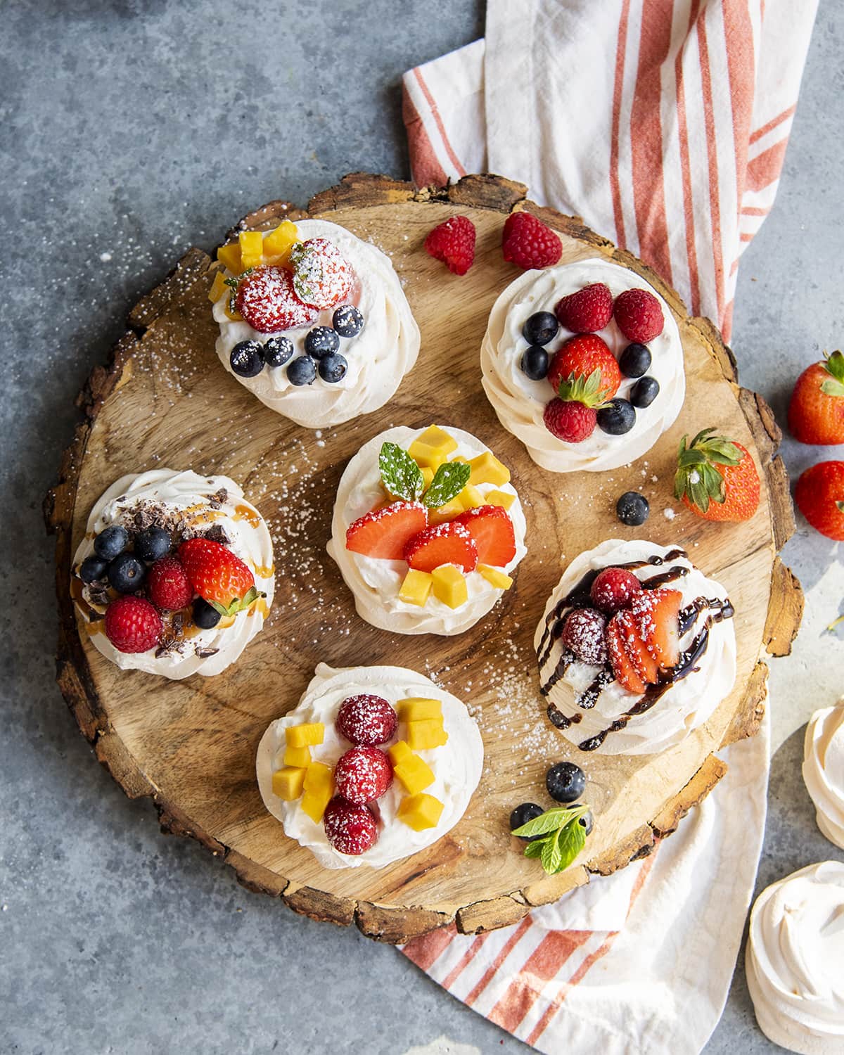 An overhead photo of a platter with mini pavlovas decorated with different fruits.